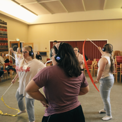 En dansegruppe, alle har på seg headset og bruker gymnstikkbånd